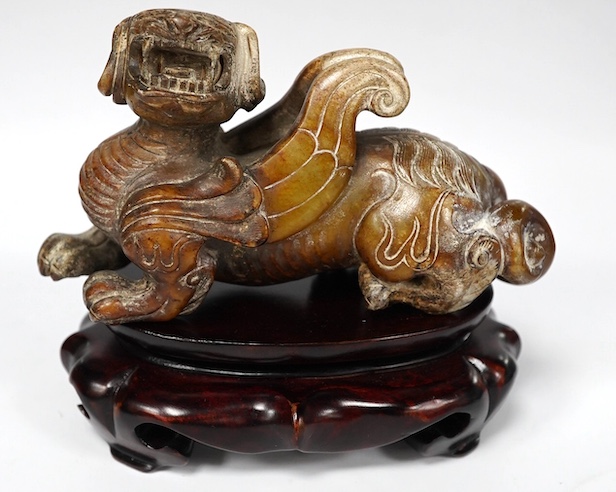 A Chinese archaistic pale celadon russet and burnt jade figure of a winged mythical beast, wood stand, mythical beast 12cm wide. Condition - carving good, stand good